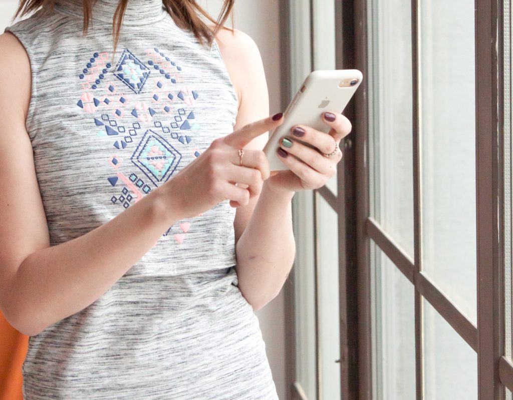 woman in gray and blue tank top holding white smartphone